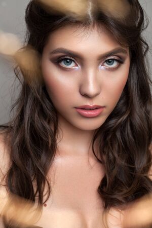 Close up photo of a beautiful young girl with professional makeup, gold eyeliner, graphic grey eyeshadows and curl hair.の写真素材