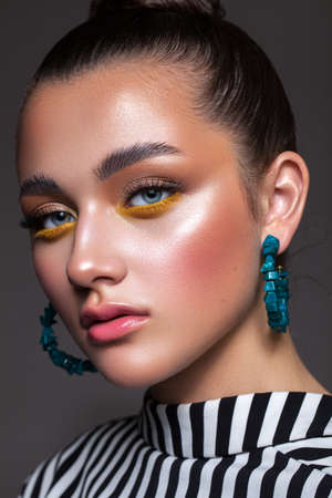 Young beautiful girl with professional make-up, fashionable multi-colored shadows and in a black and white striped blouse. The hair is gathered in a tight, smooth bun, blue-green earrings in the ears.の写真素材
