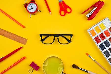 Glasses and colored school supplies on yellow desk. Top viewの写真素材
