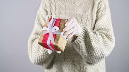 Hands in protective gloves holds a gift box with ribbon. Safe delivery for holidays.の写真素材