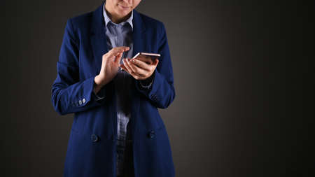 Young businesswoman in blue suit using phone. Cropped photo, isolated over grey background. Business...
