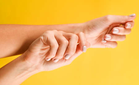Stylish fashionable female manicure in pastel colors. Hands of young girl on yellow background with festive confetti. Minimalist manicure trend.の写真素材