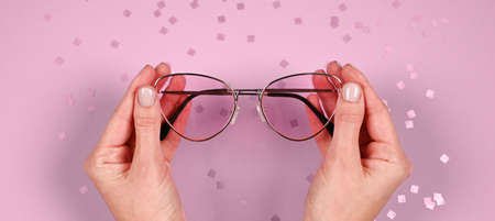 Modern pink sunglasses in female hands with pastel fingernails. Pastel violet sparkles background....