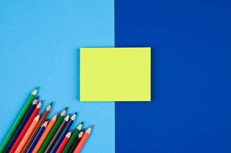 Yellow sticky notes and colored pencils on a blue surface.の写真素材