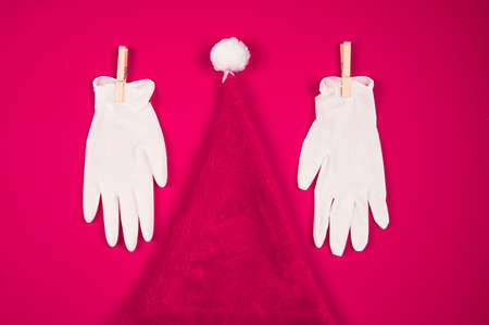 Pink christmas hat, disposable gloves on pink background with copy space. Christmas postcard during the coronavirus pandemic.の写真素材