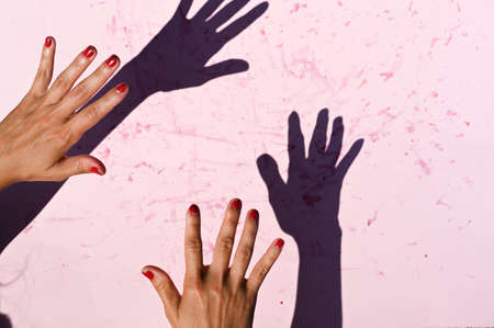 Female hands gesturing against shadow on pink background.の写真素材