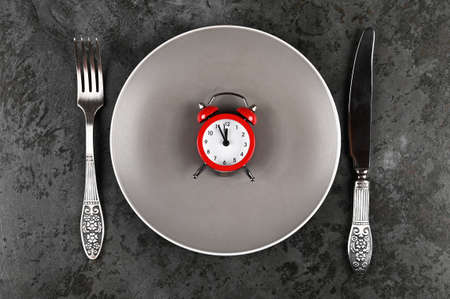 Alarm clock and plate with vintage cutlery on concrete background. Festive serving. Diet concept.の写真素材