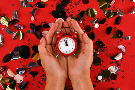 Red alarm clock in female hands is showing midnight. Festive concept.の写真素材