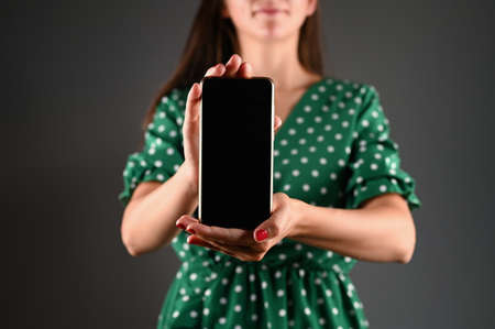 Cropped view of woman presenting smartphone with blank screen.