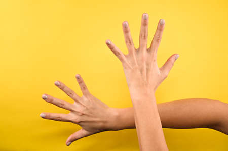 Two female hands with fingers spread wide. Short nails with pastel color manicure. Concept of advertising isolated on yellow background.の写真素材