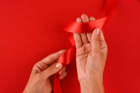 Female hands holding a red satin ribbon on a red background.の写真素材