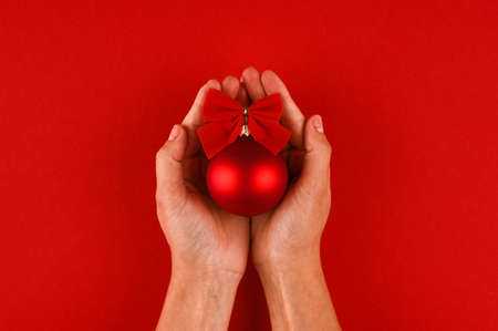 Christmas red matt ball on hands over red background, merry christmas concept.の写真素材