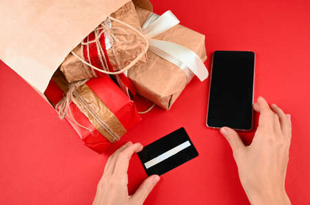 Cropped view of woman holding smartphone with blank screen with credit card and christmas gifts.の写真素材