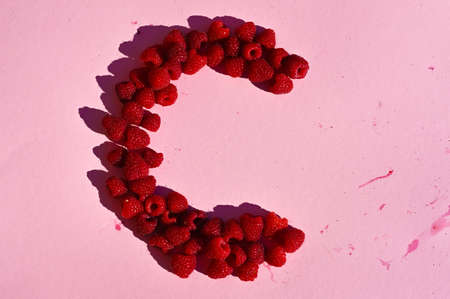 Fresh raspberries laid out in a C shape on pink background.