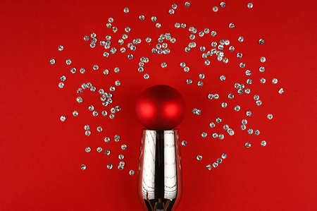 Silver champagne glass, red chrismas ball and sequins on black surface.の写真素材