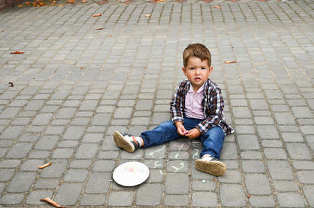 Little kid boy sitting and drawing with colored chalk on asphalt.の写真素材