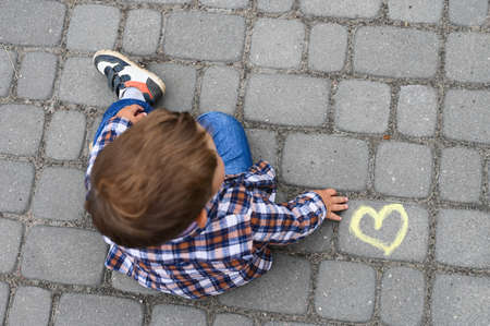 Yellow heart drawn with chalk on asphalt and a little boy next to these drawing.