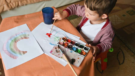 Little boy draws a rainbow on a sheet of paper in different colors. Home, game concept.の写真素材