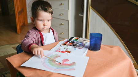 A 2 years old child draws a rainbow with paints. Creative activities at home concept. Childrens desk, drawing supplies.の写真素材