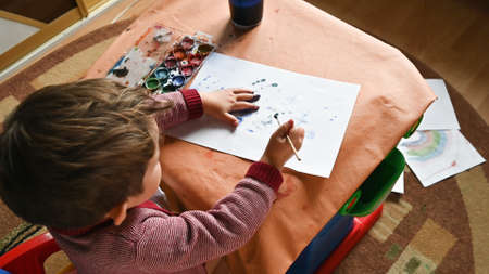 Top view little boy painting with his hands on the sheet of paper. Developing activities at home....