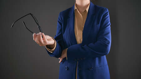 Business woman holding her glasses. Young woman in blue suit isolated on grey background.Finance and...