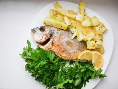 Healthy dinner or lunch with baked dorada fish or sea bream garnished with parsley on white...