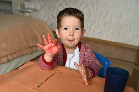 Happy boy showing hand in paint. Portrait of cute brunet boy at home. Child playing with paints