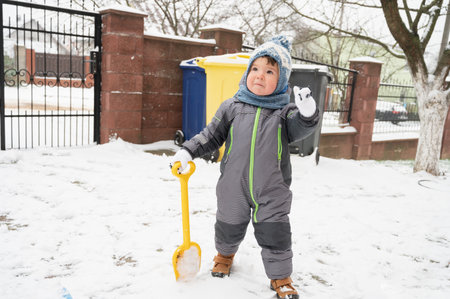 A cute toddler baby outdoors on snow background. Boy playing with a shovel outdoors. Little helper concept.の写真素材