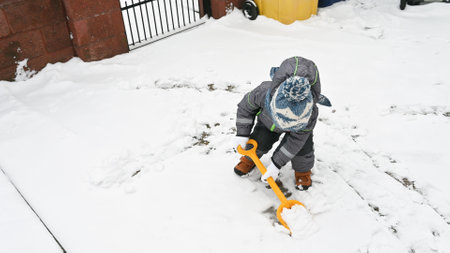 Little boy with a shovel playing outside in the snow. Toddler baby in warm clothes. Little helper conceptの写真素材