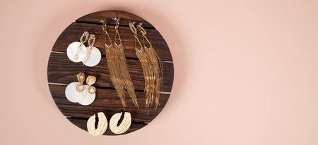 Stylish female jewelry on dark wooden stand on pink background. Fashion and style concept. Top view of golden earrings. High quality photoの写真素材