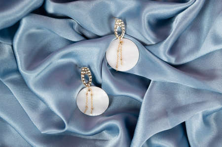 Stylish trendy golden earrings on crumpled blue fabric bacground. Fashionable women's jewelry with shell rock. High quality photoの写真素材