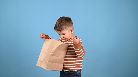 Cute toddler boy with paper bag on blue background. Caucasian two years old boy holding shopping bag. Sales concept.の写真素材