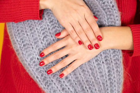 Female hands manicure close up view on gray knitted hat background. Manicure salon concept. Winter...