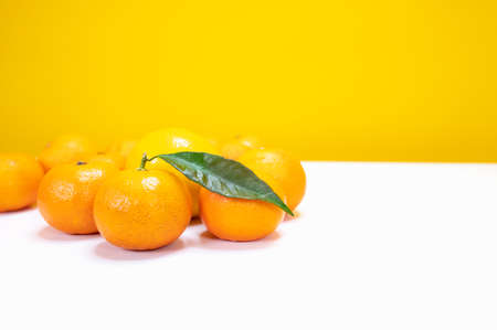 Fresh tangerines on a white table. Side view. Yellow background with copy space. High quality photoの写真素材