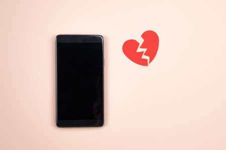 Smartphone with empty screen and broken red paper heart on pink background. Parting, unrequited love concept ,. High quality photoの写真素材