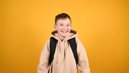 Happy adorable boy laughing. Handsome young boy 10s in streetwear hoodie isolated on yellow...