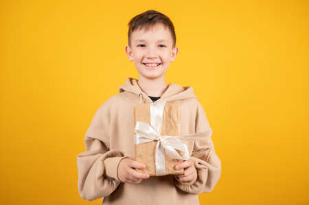 Cute happy boy holding gift box on yellow background. Celebrate new year, valentines day. Birthday gift. Birthday boy. Buy gifts. High quality photoの写真素材