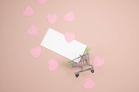 The pink paper hearts and empty blank card flying from shopping cart on pastel pink background. Shopping on valentines day concept. High quality photoの写真素材