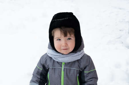 Portrait of smilling little toddler boy in warm clothes, playing outdoors with snow on a winter....