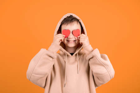 Close-up portrait of cheerful teen boy holding in hands two small little hearts. Young boy hide his...