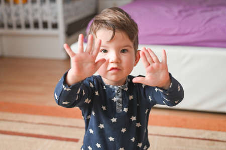 Smart cute child counts fingers. A beautiful kid shows his hand, a small palm. Caucasian boy on a bedroom background. High quality photoの写真素材