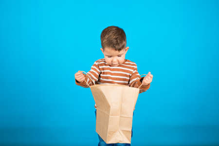 Baby boy looking inside paper bag. Toddler with shopping bag on blue background. Shopping and sales...