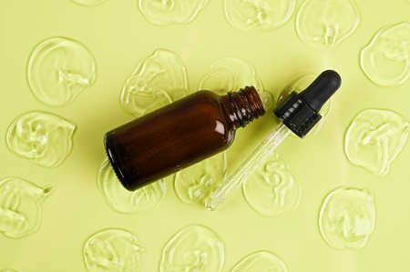 Bottle of cosmetic serum with pipette on green background with drops of gel. Cosmetics concept. High...