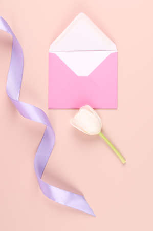 White tulip, silk ribbon and pink envelope on pastel pink background. Mockup with white card. Flat...