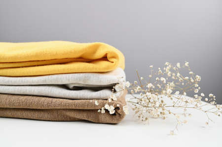 Stack knitted sweaters in pastel colors and branch of white gypsophila lie on white table. Warm comfortable clothes. Delicate care for knitted clothing concept. High quality photoの写真素材