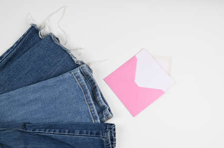Cropped view of denim Jeans and pink envelope with blank card isolated on white. Shopping and sales...