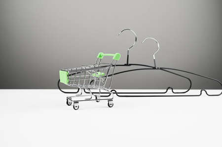 Mini shopping cart and black metal hangers, side view. Store concept, sale, design, empty hanger. High quality photoの写真素材