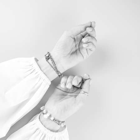 Cropped view of tender female hands with stylish silver bracelets in a white shirt with voluminous sleeves. Black and white image, top view. High quality photoの素材 [FY310165196046]