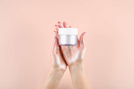 Top view of female hands holding matt glass jar of cream. Tender hands painted with highlighter. Skin care concept. High quality photoの写真素材