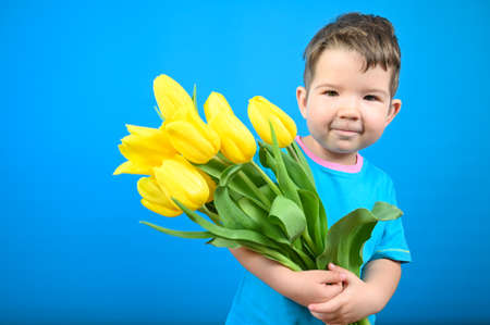 Cute little boy with a bouquet of yellow tilips is ready to congratulate with a holiday. High quality photoの写真素材
